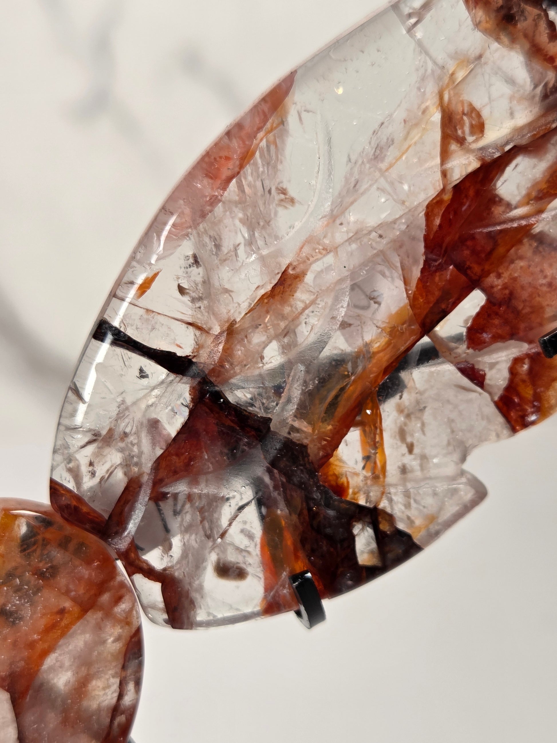 A close-up of a clear teardrop-shaped gemstone or crystal pendant with internal brown and amber inclusions, photographed against a light neutral background.