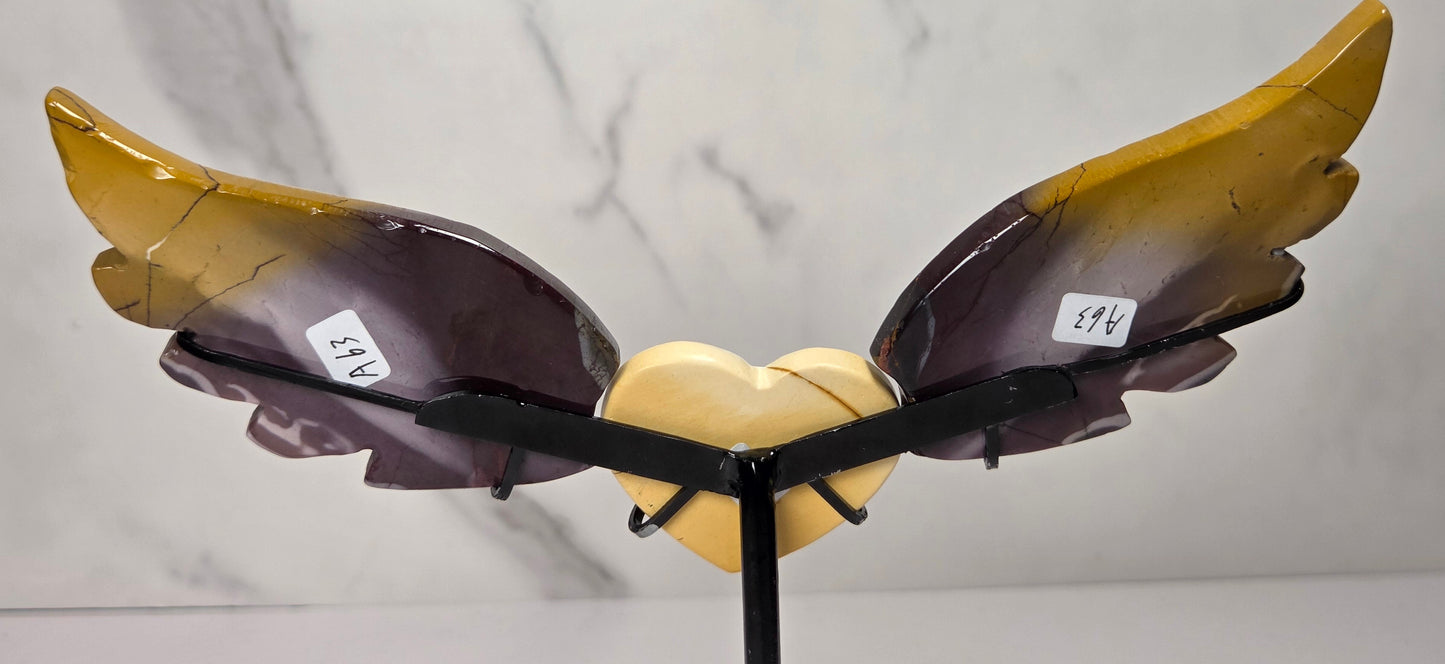 A decorative winged heart sculpture with a glossy amber-yellow and dark purple gradient finish, mounted on a black stand against a light gray marble-patterned background.