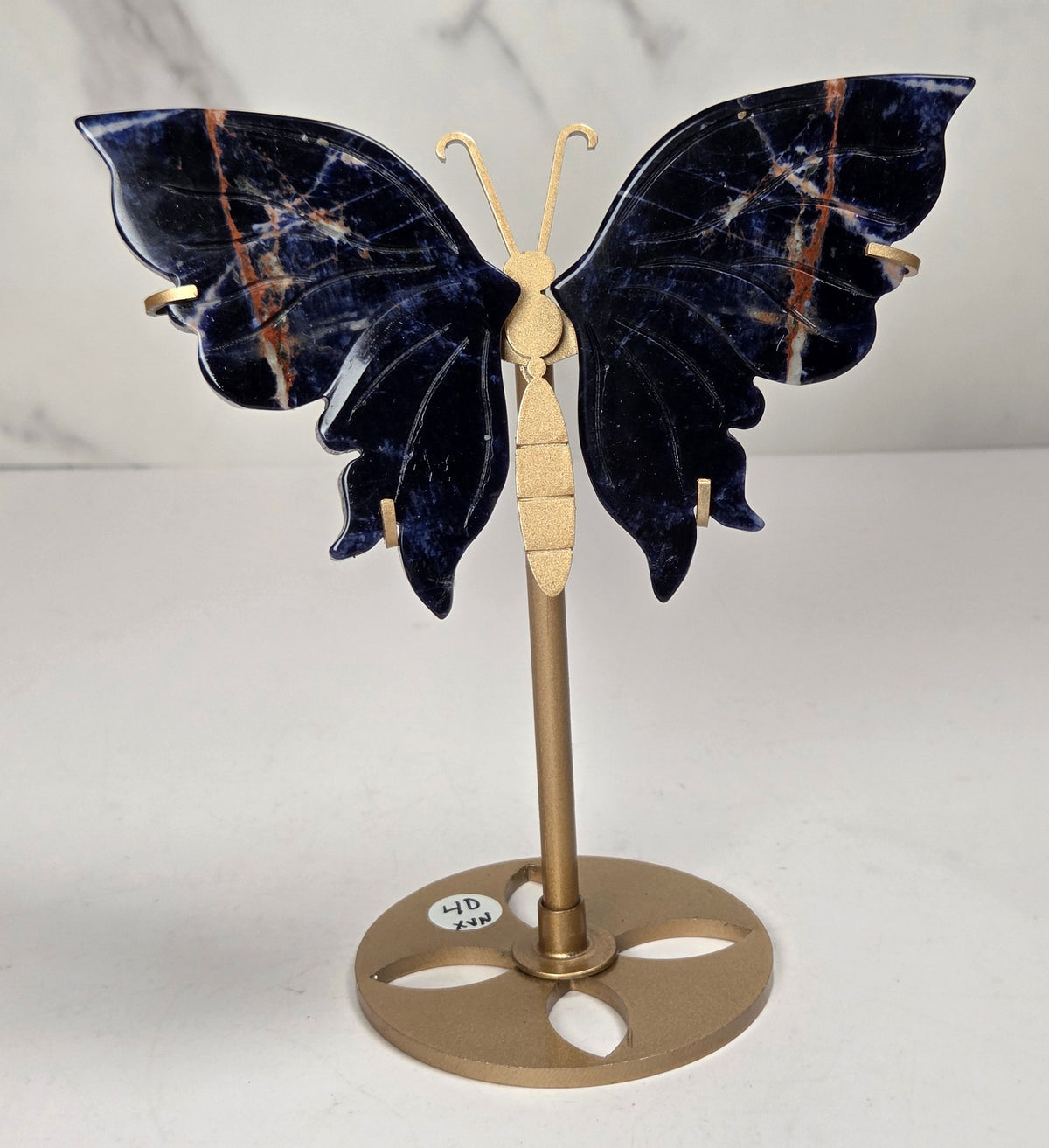A butterfly-shaped jewelry display stand made of deep blue lapis lazuli stone with gold-toned metal accents, shown on a light marble background.