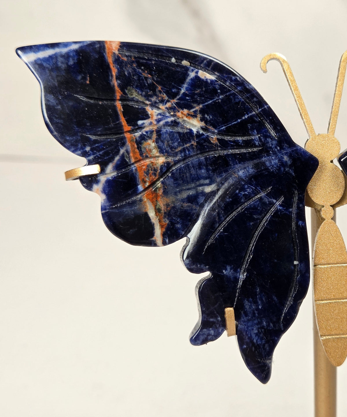 A butterfly-shaped jewelry display stand made of deep blue lapis lazuli stone with gold-toned metal accents, shown on a light marble background.