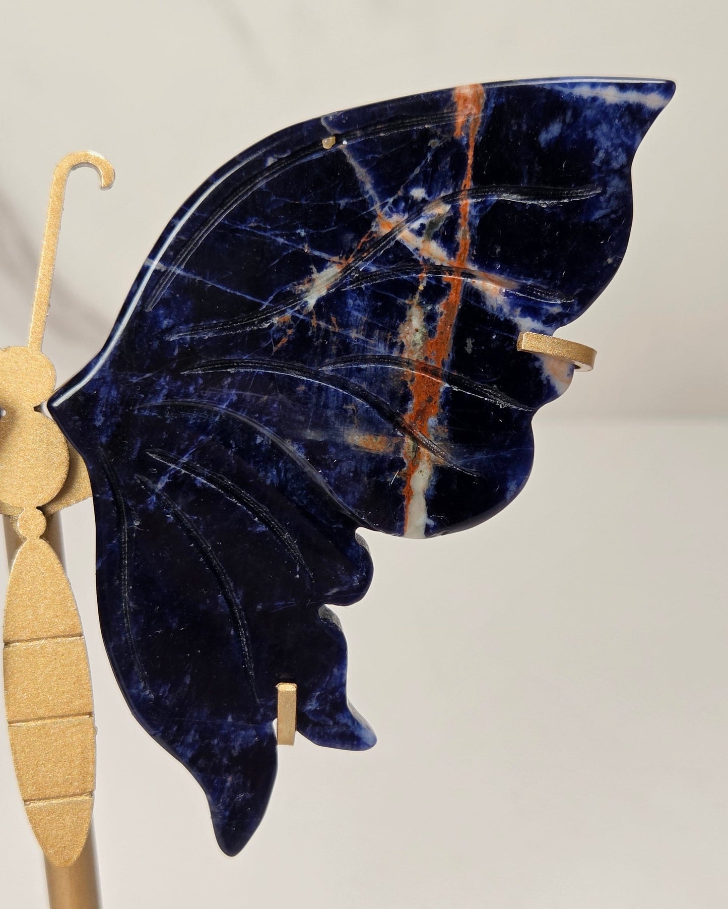 A butterfly-shaped decorative piece made from deep navy blue stone with natural veining and small orange-brown inclusions, mounted on a gold-toned metal stand against a light neutral background.