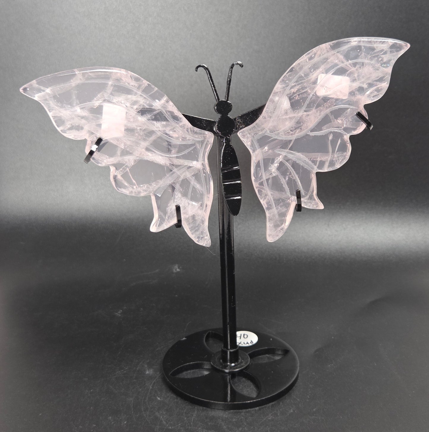 A butterfly-shaped decorative sculpture or wall art piece with translucent pale pink wings and a black stand, photographed against a dark gray studio backdrop.