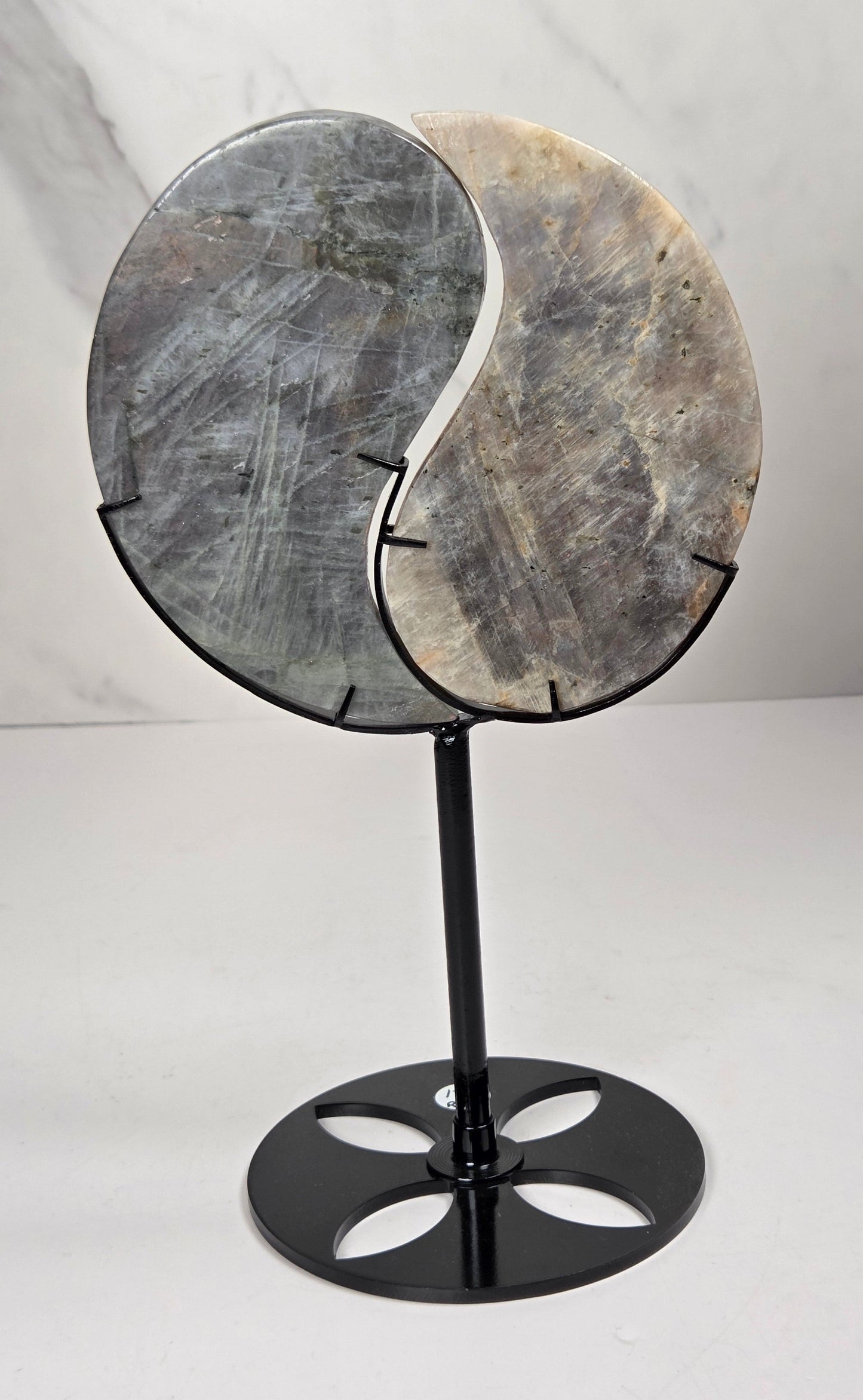 yin yang symbol carved out of two different crystals, set in a black stand against a marbled background