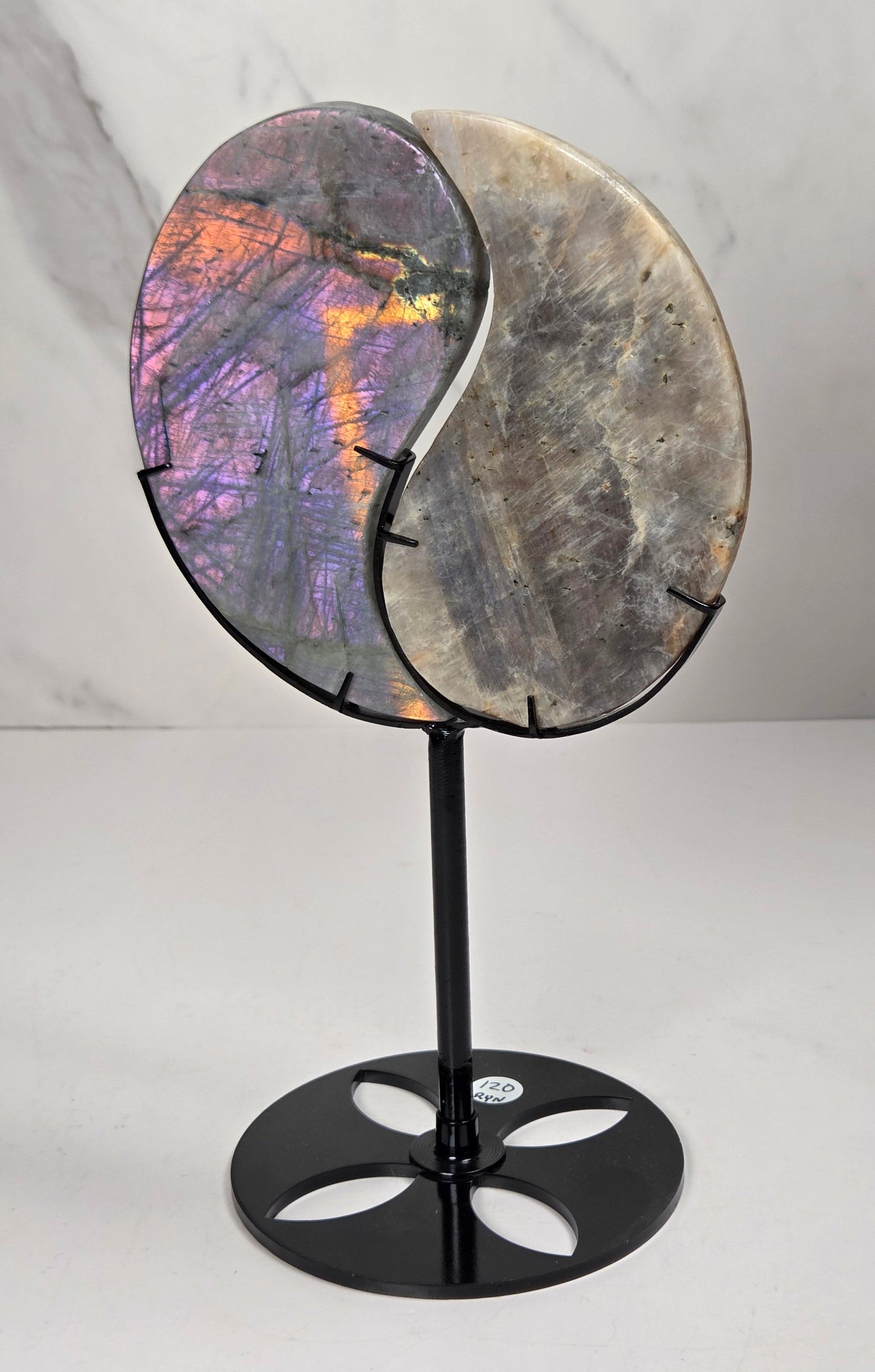 yin yang symbol carved out of two different crystals, set in a black stand against a marbled background