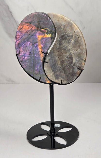 yin yang symbol carved out of two different crystals, set in a black stand against a marbled background