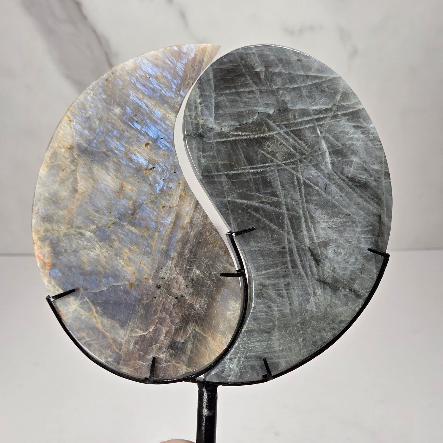 yin yang symbol carved out of two different crystals, set in a black stand against a marbled background