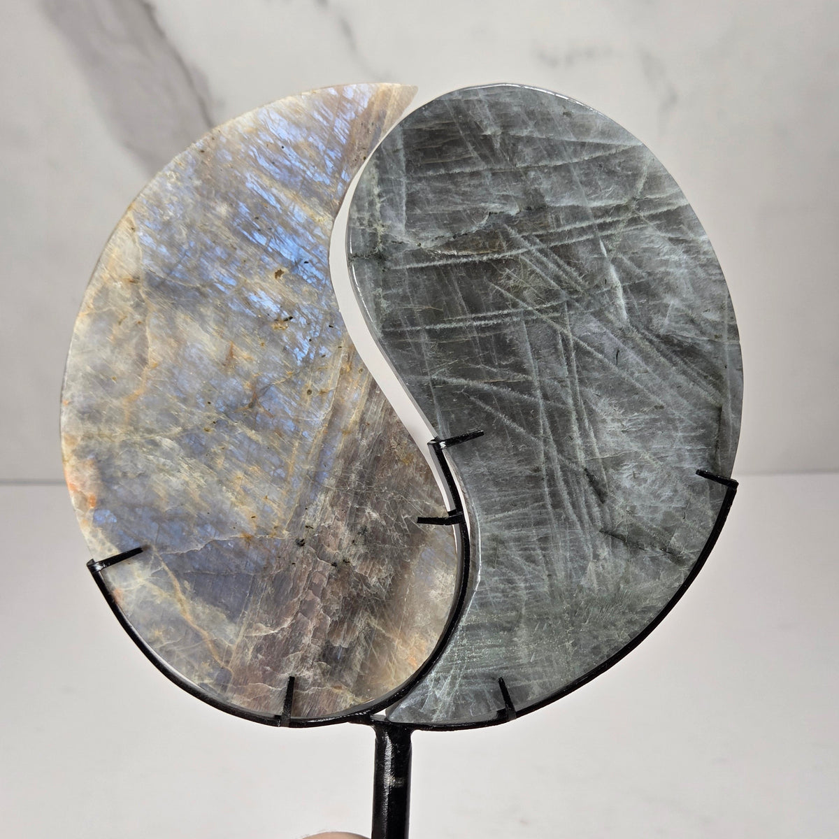 yin yang symbol carved out of two different crystals, set in a black stand against a marbled background