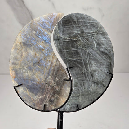 yin yang symbol carved out of two different crystals, set in a black stand against a marbled background