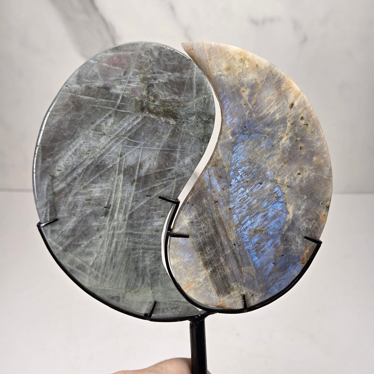 yin yang symbol carved out of two different crystals, set in a black stand against a marbled background
