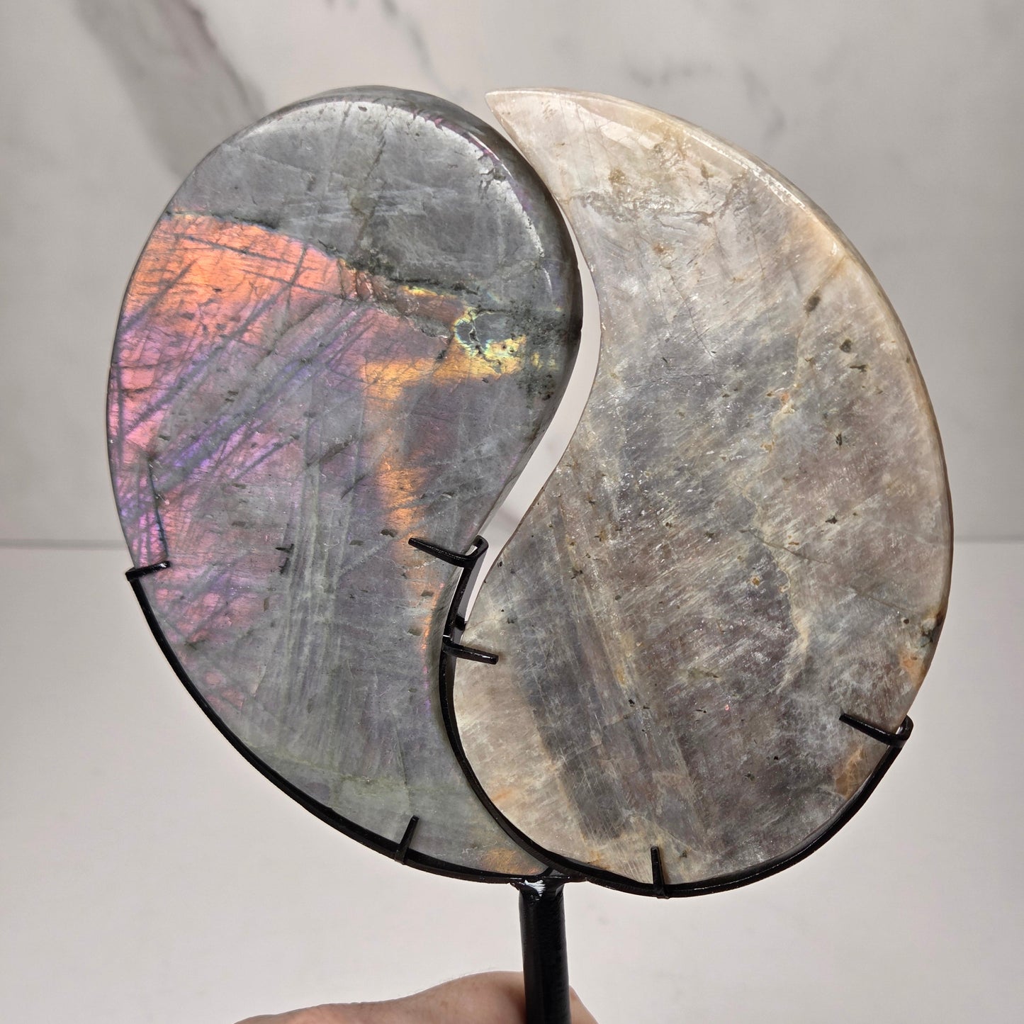 yin yang symbol carved out of two different crystals, set in a black stand against a marbled background