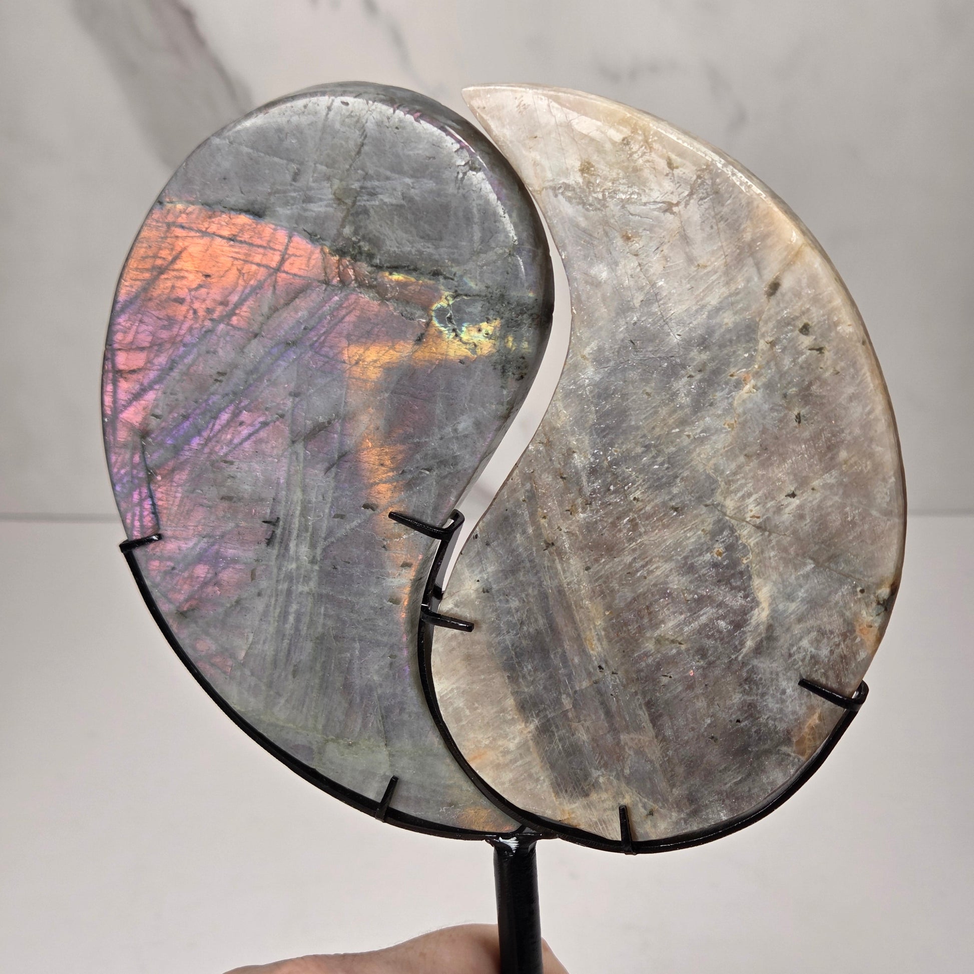 yin yang symbol carved out of two different crystals, set in a black stand against a marbled background