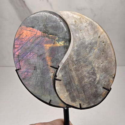 yin yang symbol carved out of two different crystals, set in a black stand against a marbled background