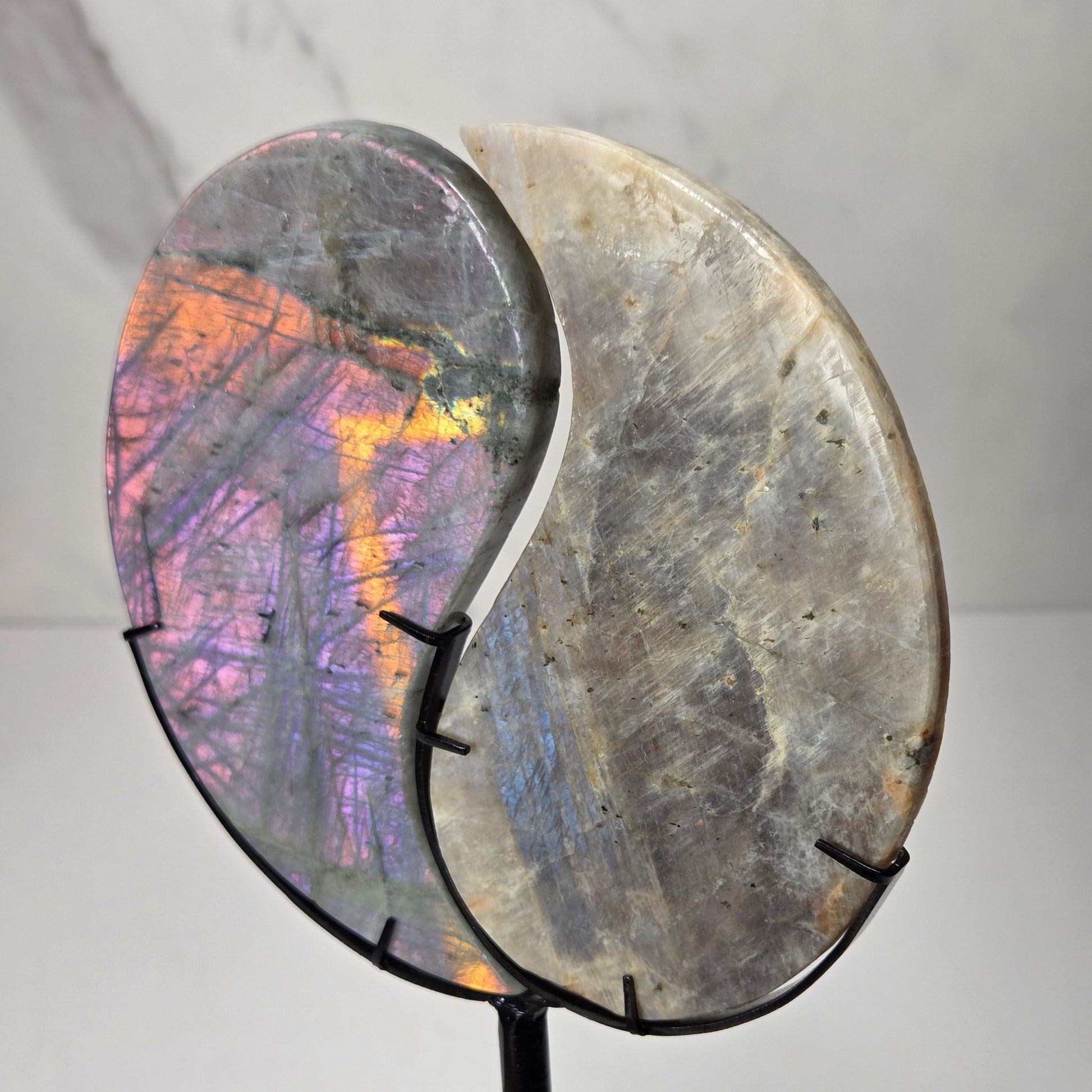yin yang symbol carved out of two different crystals, set in a black stand against a marbled background