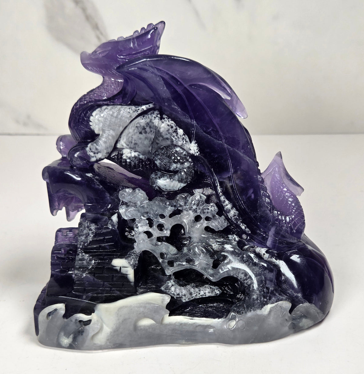 Intricately carved fluorite dragon with purple and white coloring against a marbled background