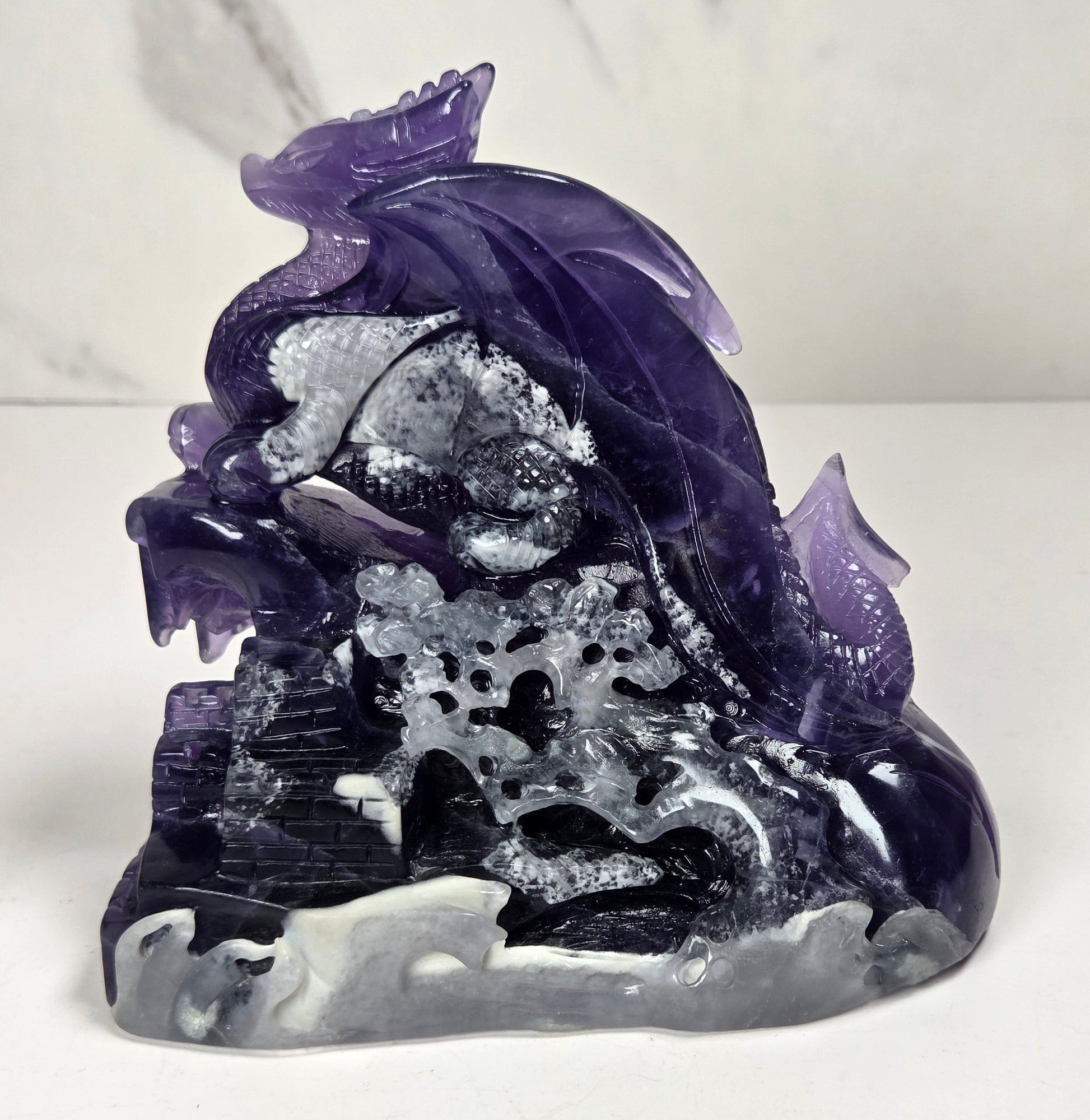 Intricately carved fluorite dragon with purple and white coloring against a marbled background