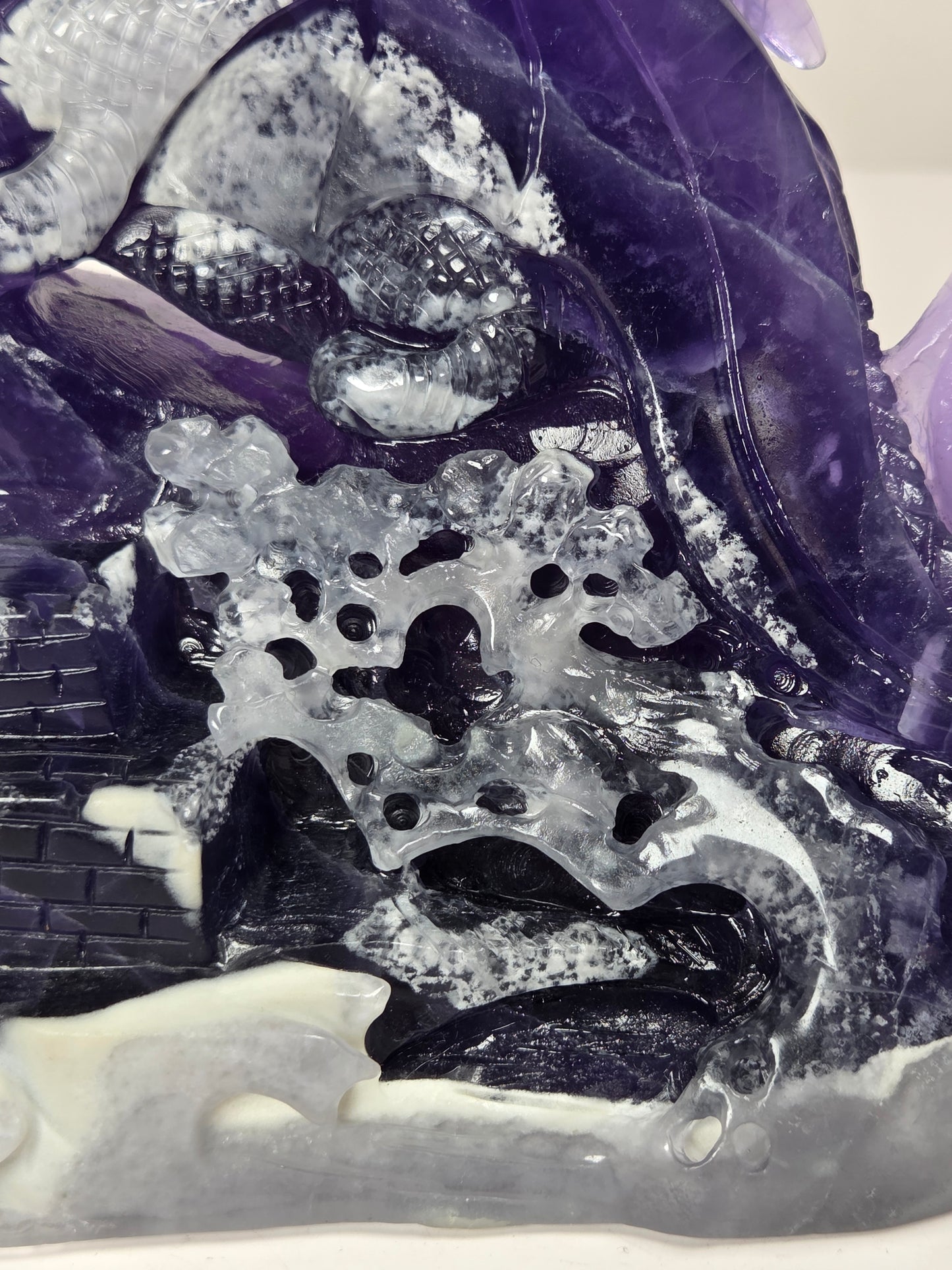 Close-up of a Intricately carved fluorite dragon with purple and white coloring against a marbled background