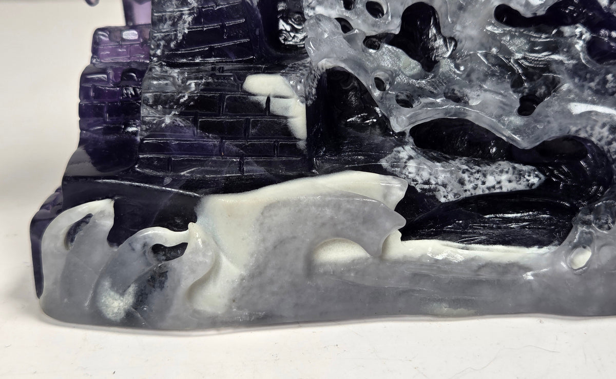 A close-up of a carved stone sculpture depicting a mountainous landscape with dark purple, black, gray, and white marbled stone.