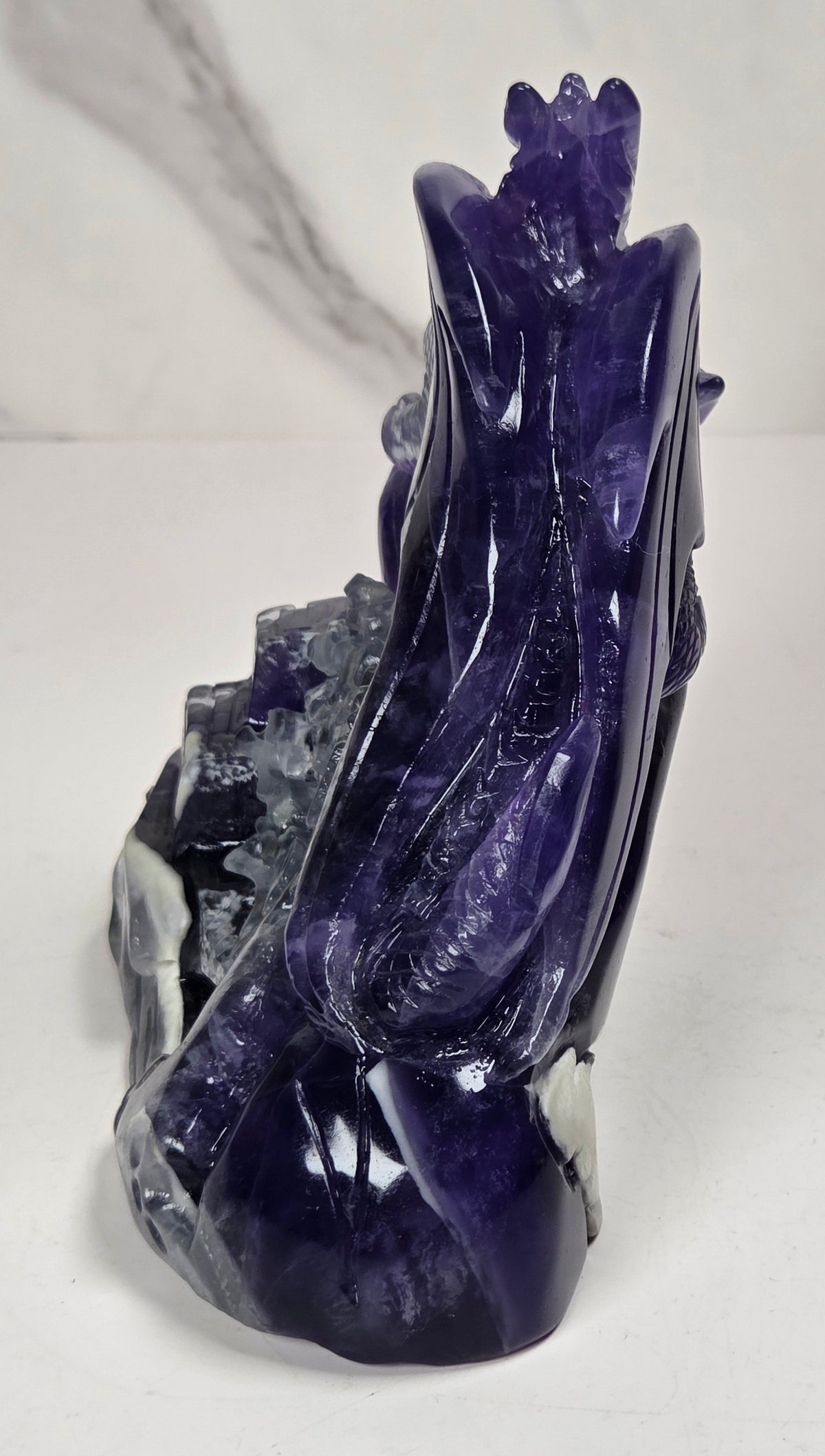 Intricately carved fluorite dragon with purple and white coloring against a marbled background