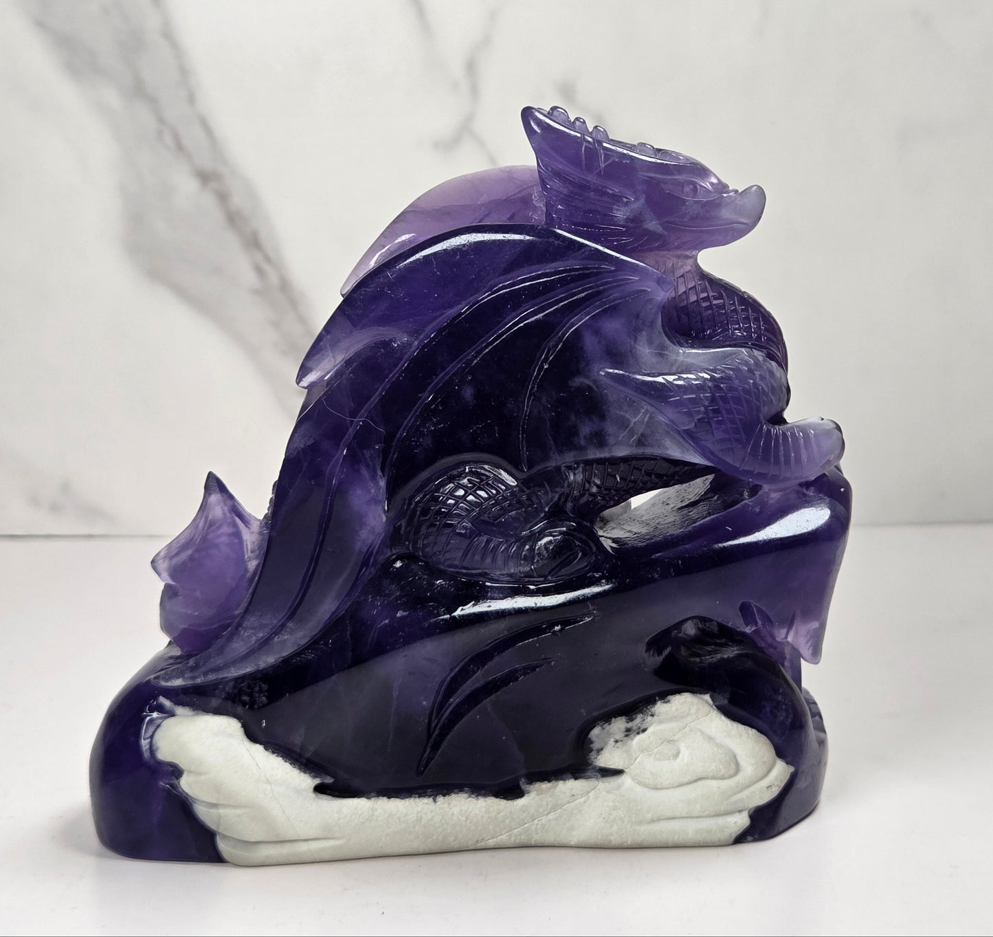 Intricately carved fluorite dragon with purple and white coloring against a marbled background