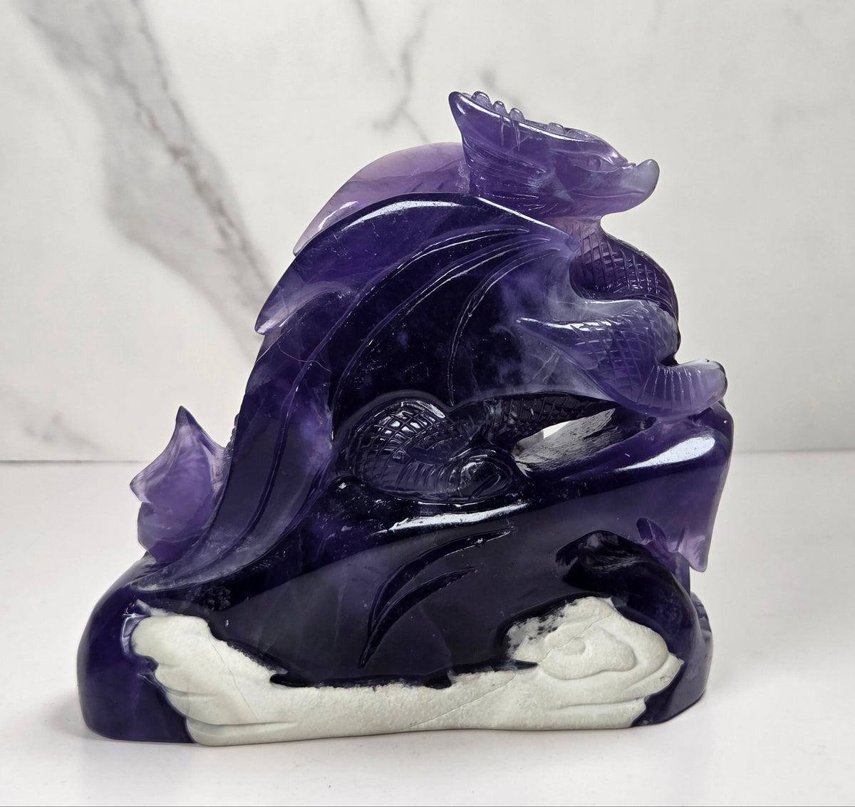 Intricately carved fluorite dragon with purple and white coloring against a marbled background
