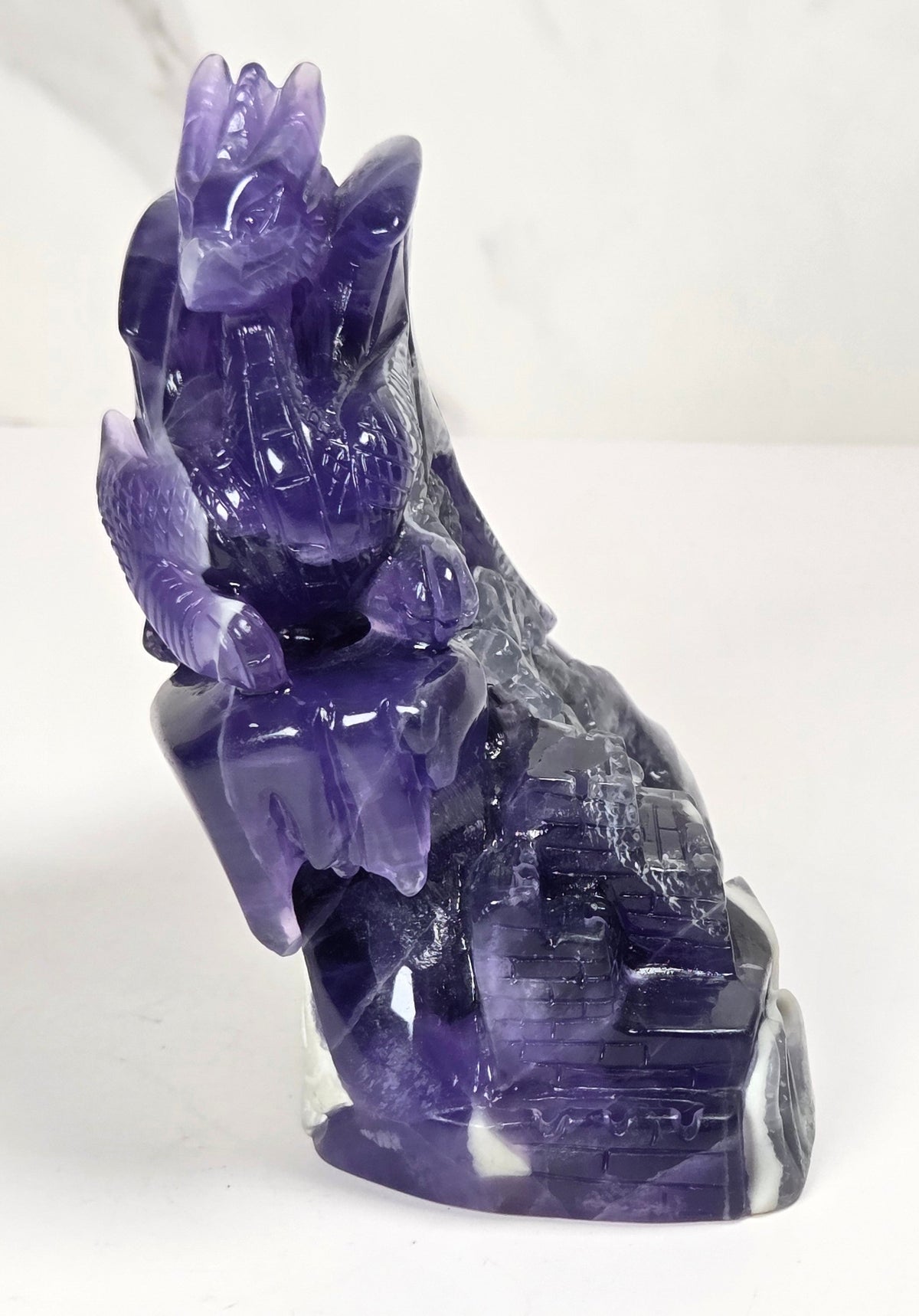 Intricately carved fluorite dragon with purple and white coloring against a marbled background