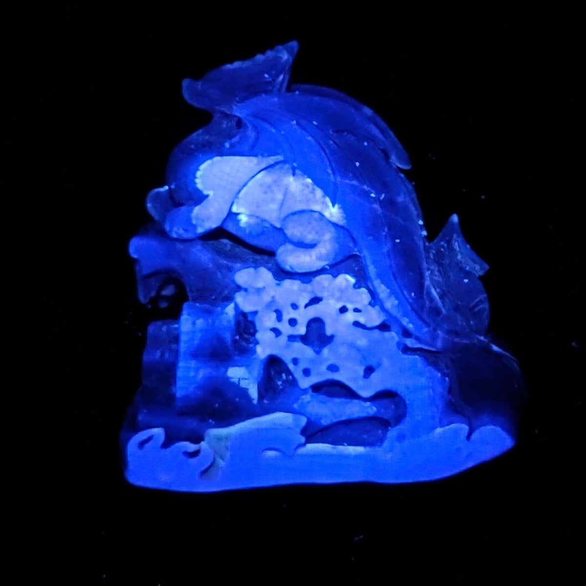 A carved translucent blue stone figurine, possibly depicting a sea creature or decorative sculpture, shown glowing against a solid black background.