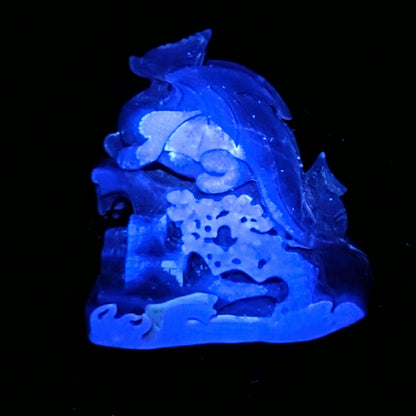A carved translucent blue stone figurine, possibly depicting a sea creature or decorative sculpture, shown glowing against a solid black background.