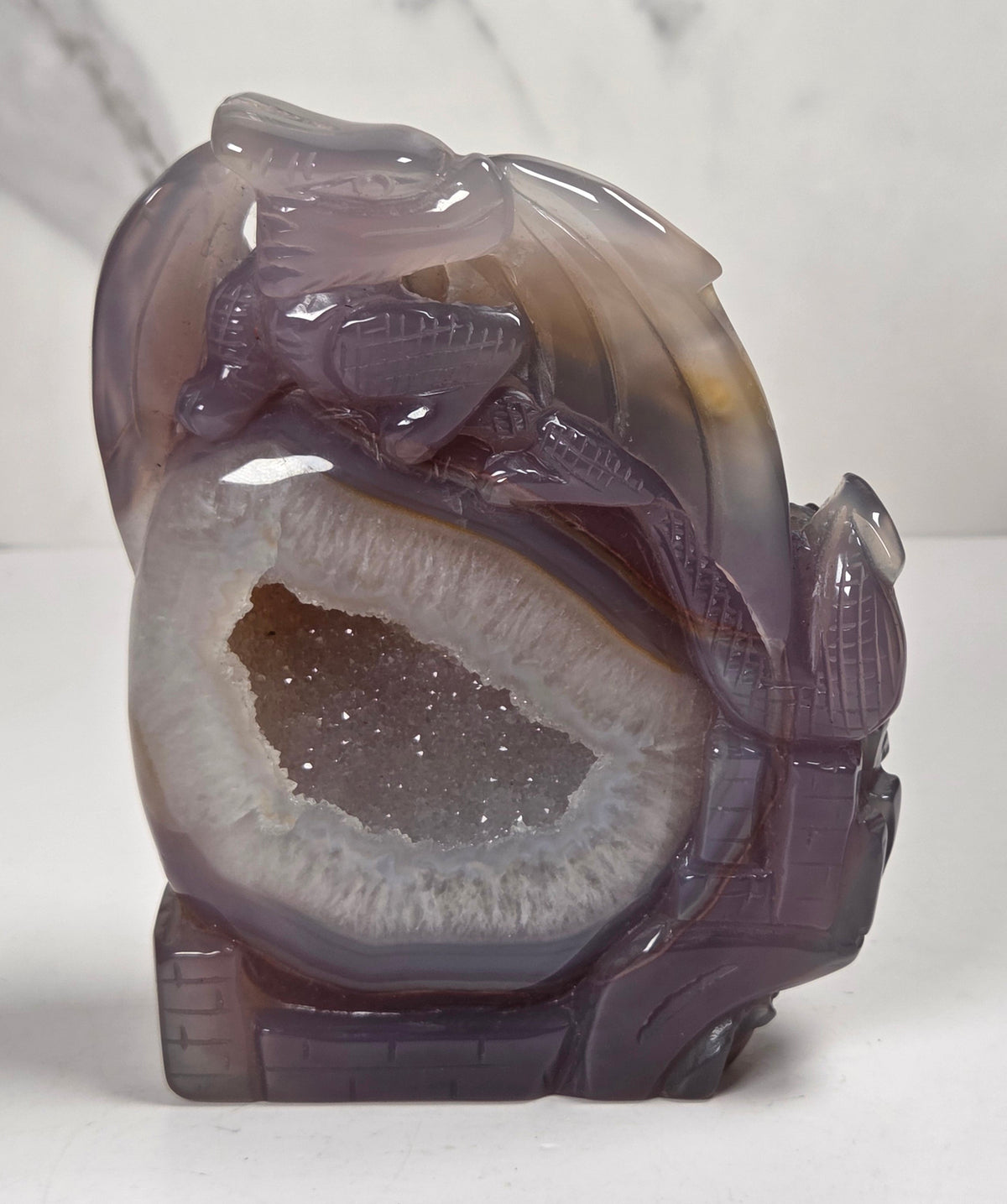 druzy agate carved dragon with a crystal pocket against a marbled background