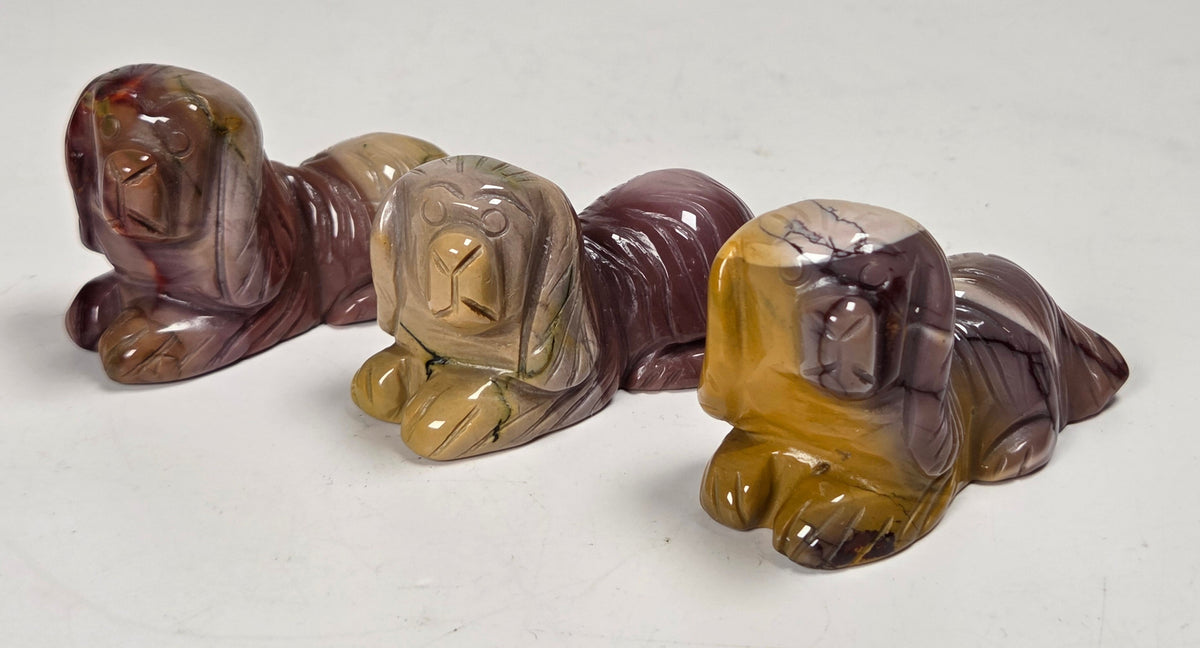 Mookaite crystal carved into dog shapes with red, yellow and tan coloring against a white background