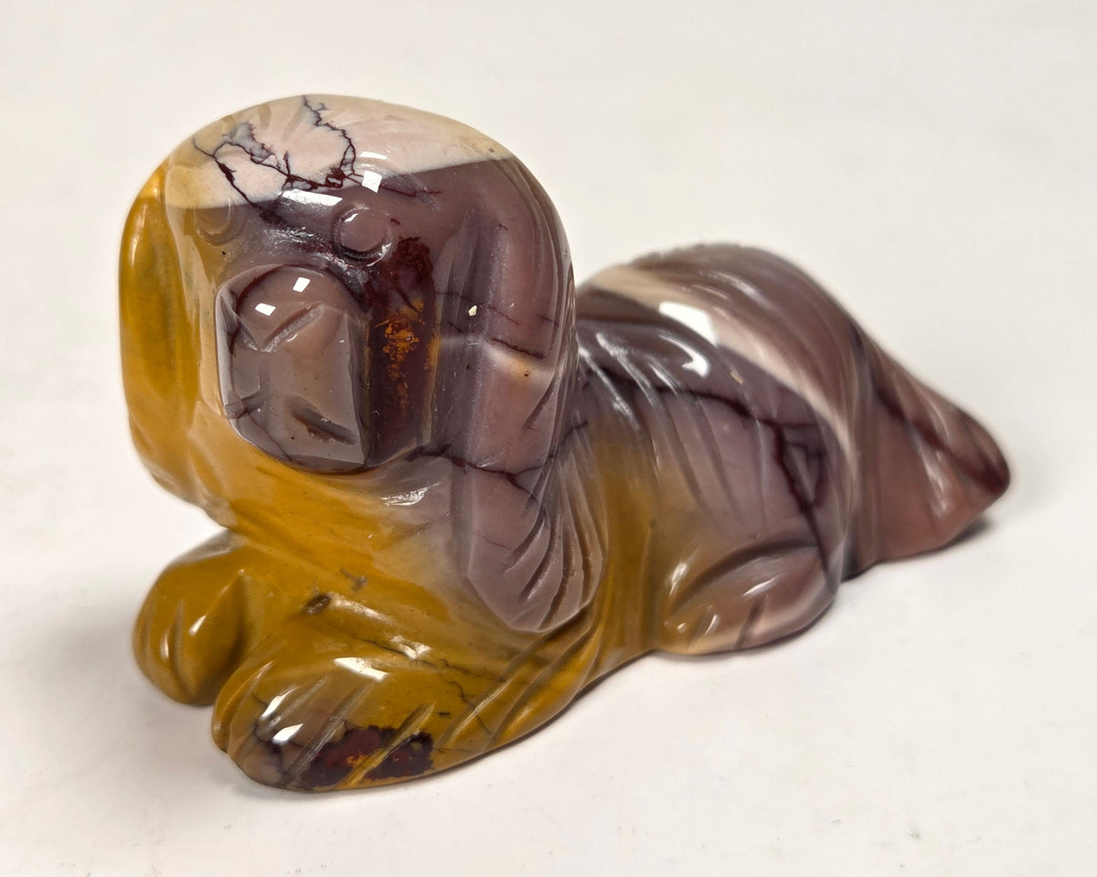 Mookaite crystal carved into a dog shape with red, yellow and tan coloring against a white background