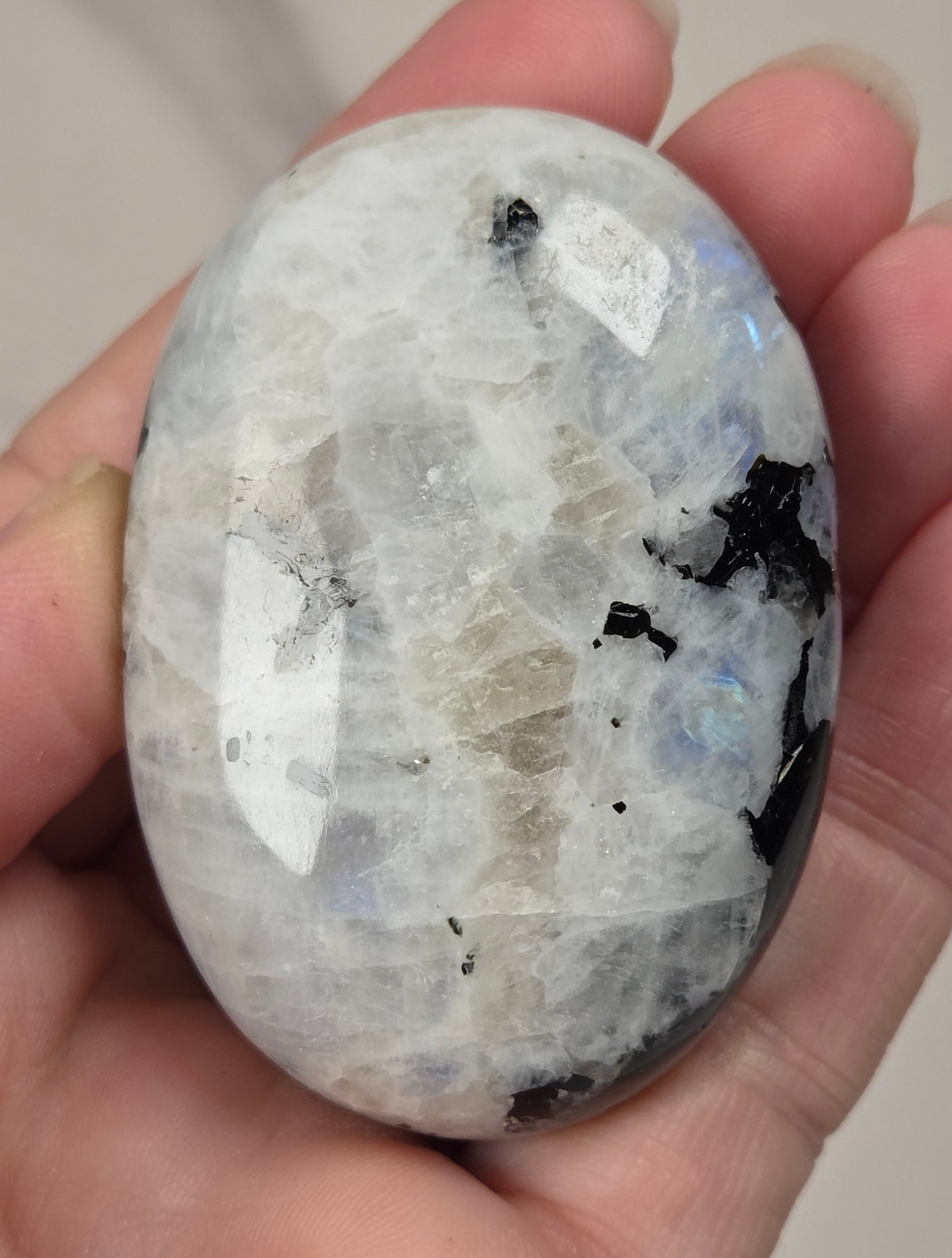 hand holding a white crystal palm carving with black and brown inclusions and some blue flash on a white background