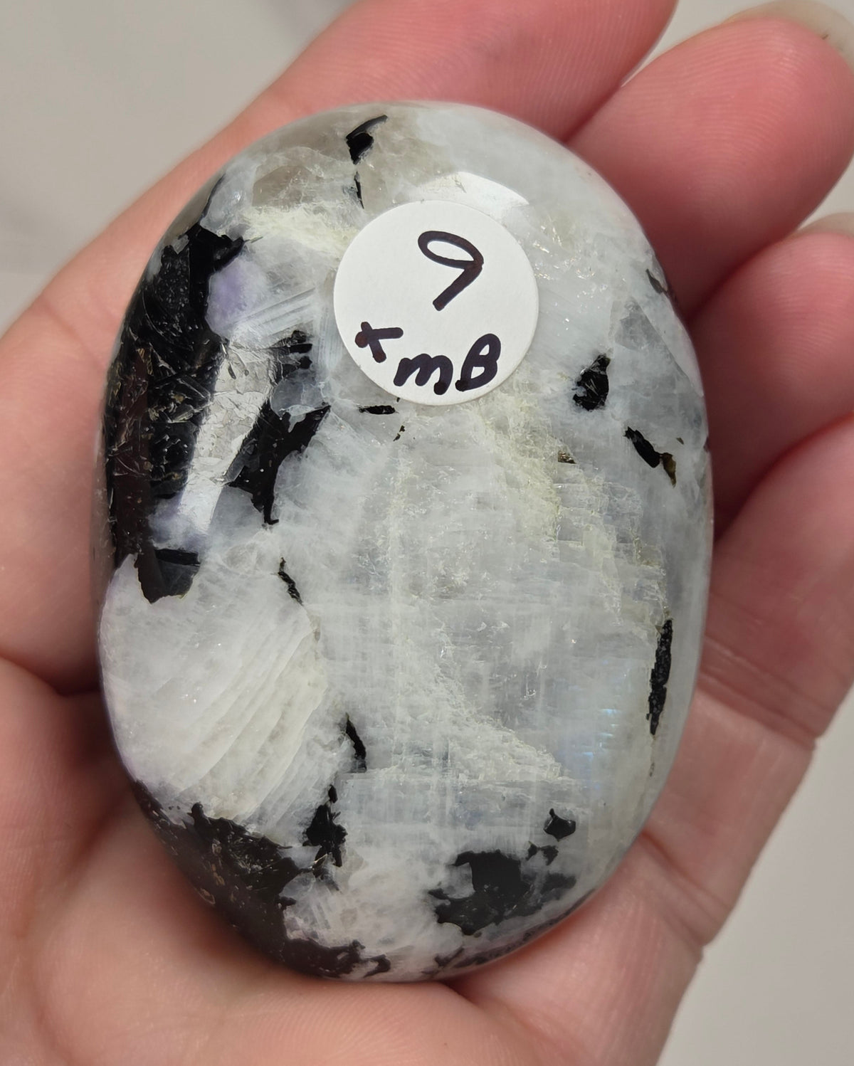 hand holding a white crystal palm carving with black and brown inclusions and some blue flash on a white background