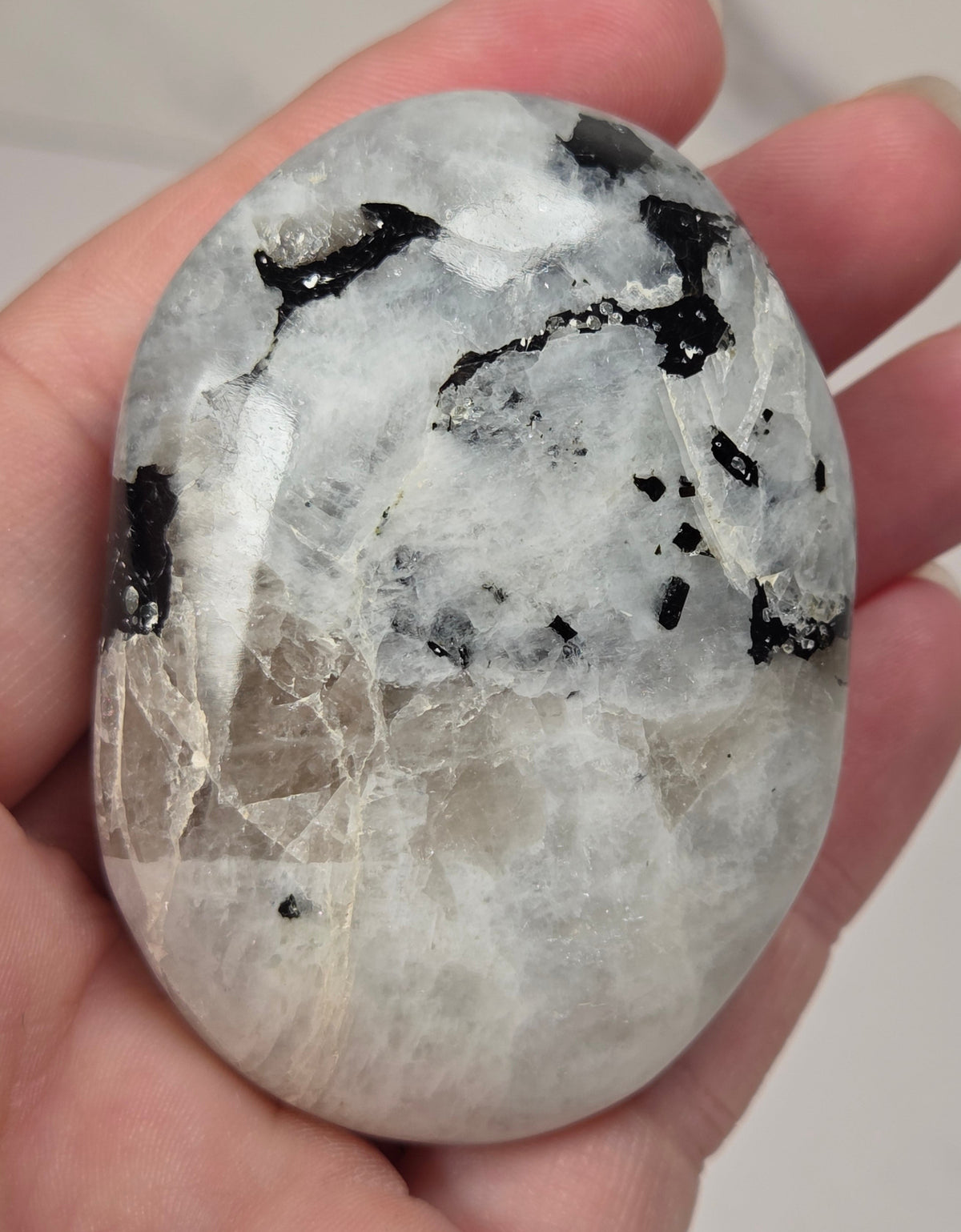 hand holding a white crystal palm carving with black and brown inclusions and some blue flash on a white background