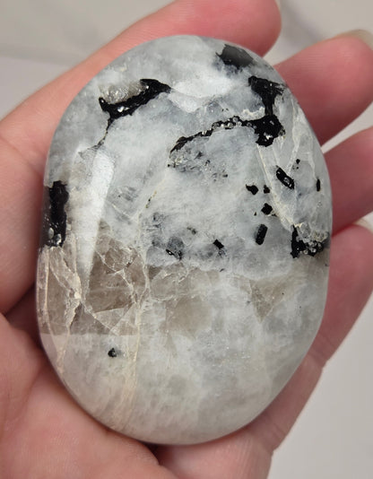 hand holding a white crystal palm carving with black and brown inclusions and some blue flash on a white background