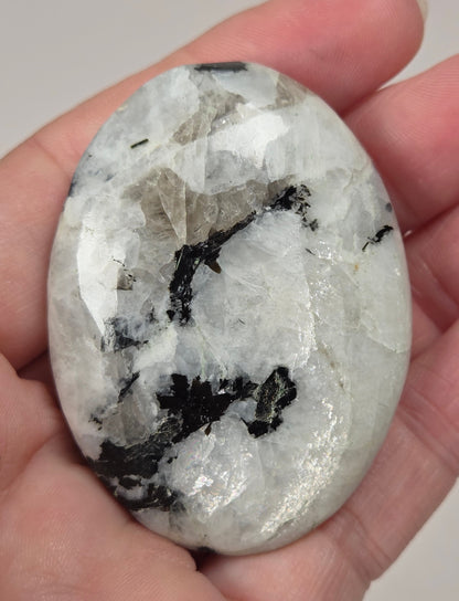 hand holding a white crystal palm carving with black and brown inclusions and some blue flash on a white background