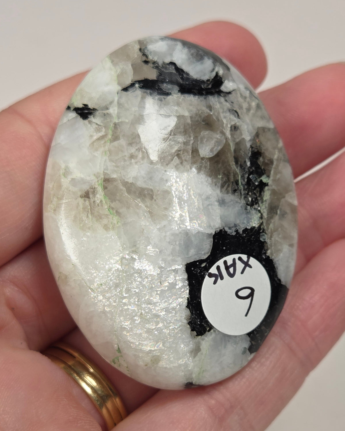 hand holding a white crystal palm carving with black and brown inclusions and some blue flash on a white background