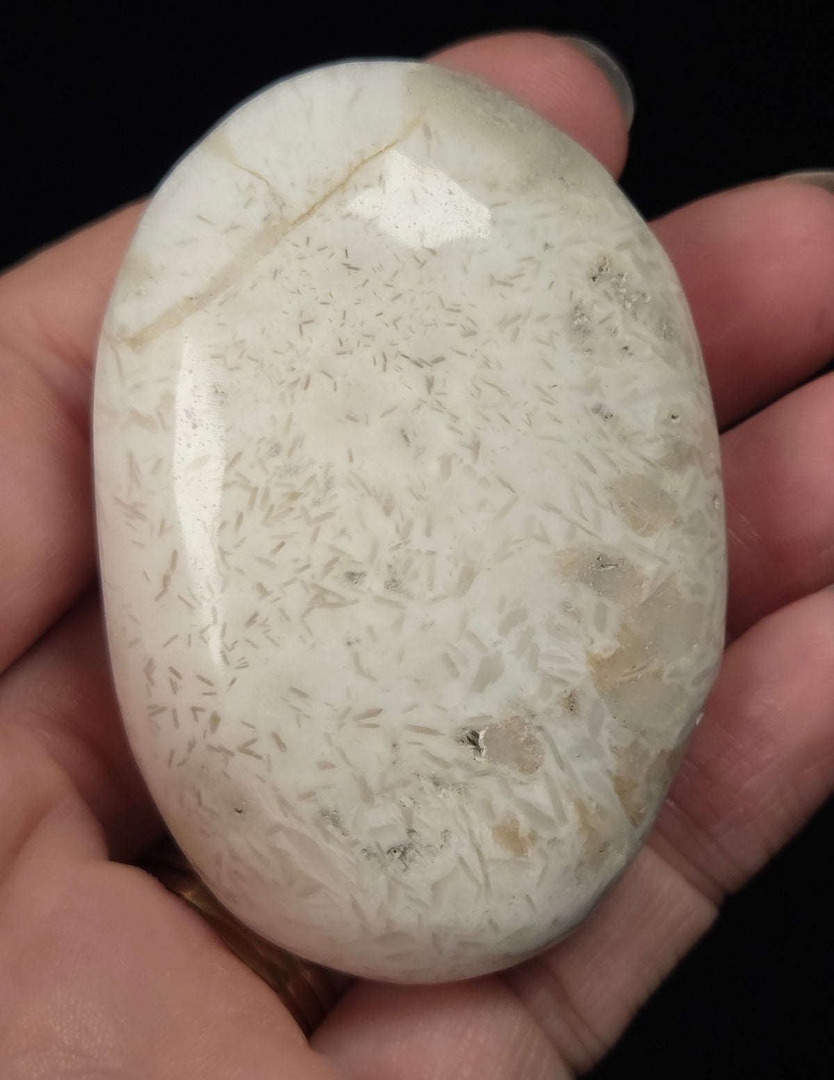 white crystal palm carving being held in a hand against a black background