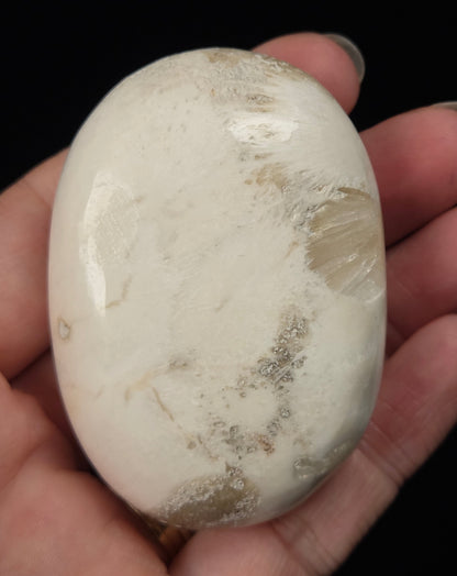 white crystal palm carving being held in a hand against a black background