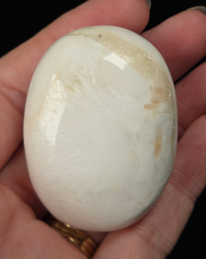 white crystal palm carving being held in a hand against a black background