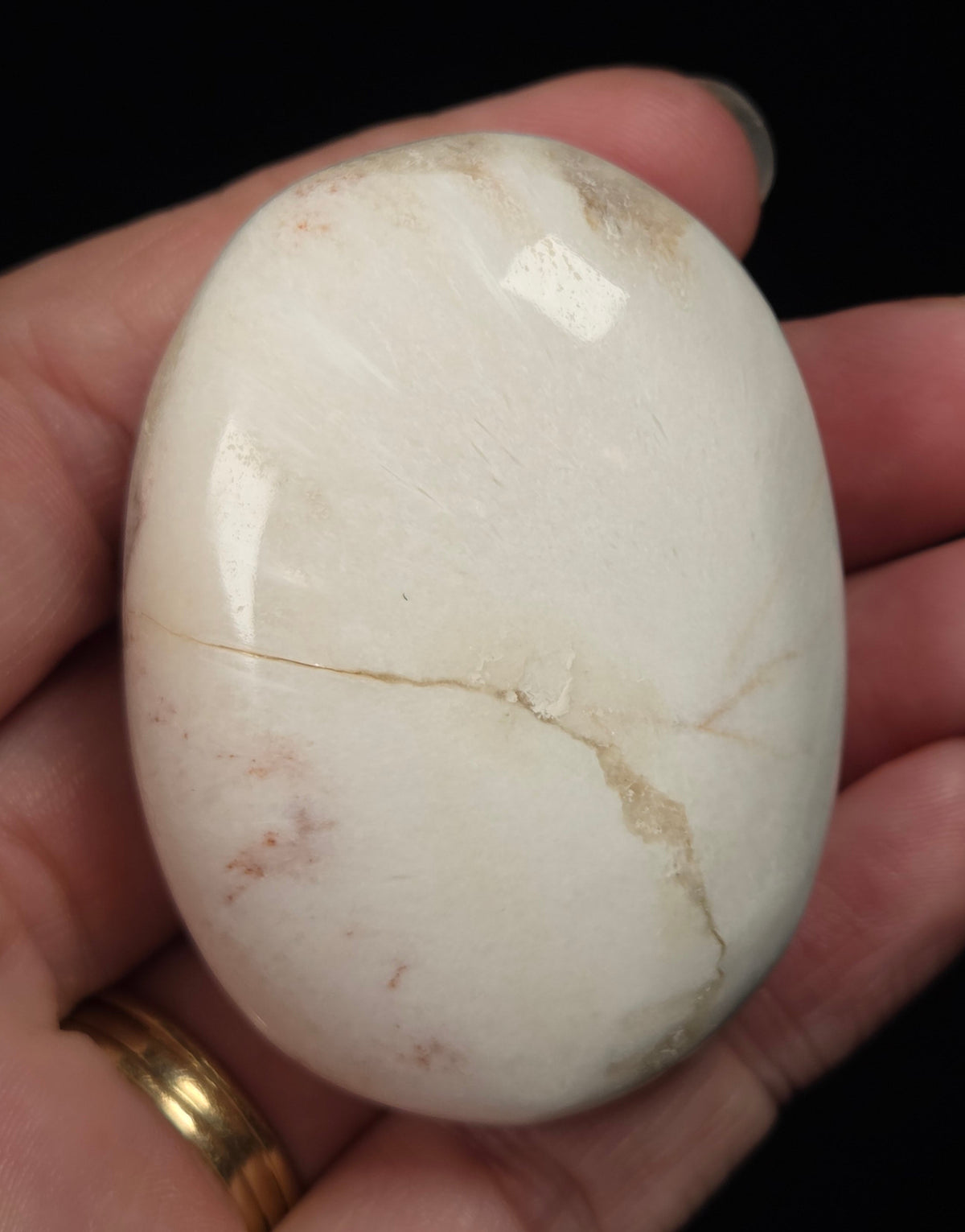 white crystal palm carving being held in a hand against a black background