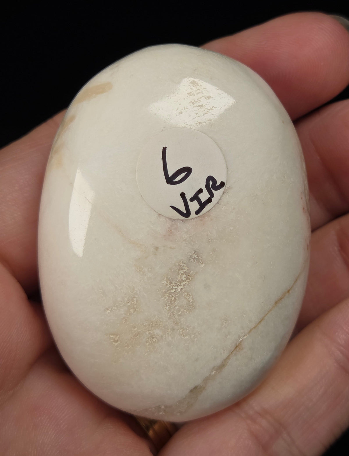 white crystal palm carving being held in a hand against a black background