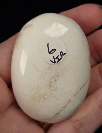 white crystal palm carving being held in a hand against a black background