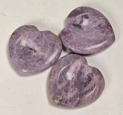 heart shaped lepidolite crystal carvings against a white background