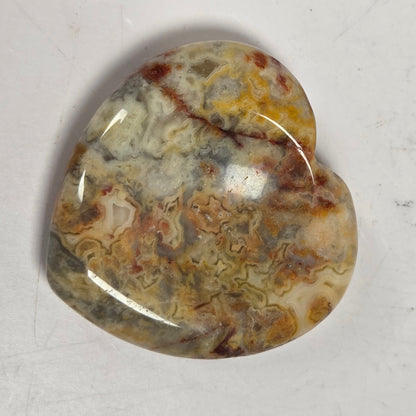 heart shaped crystal carving with tan, yellow and red marbled coloring against a white background