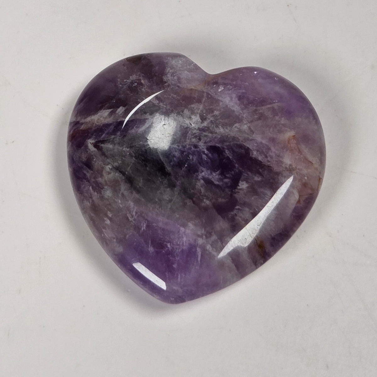 heart shaped amethyst crystal carving against a white background