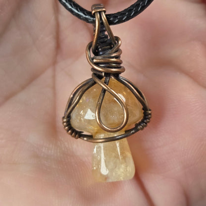 A mushroom-shaped pendant made of milky white stone wrapped in copper wire, hanging from a black cord and held in a person's hand.