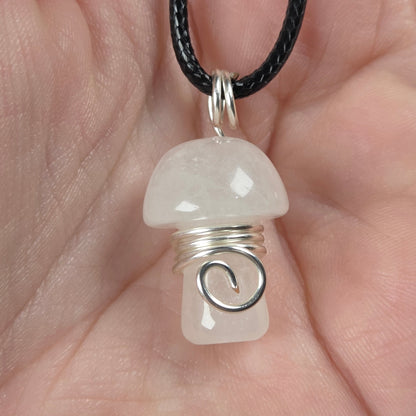 A mushroom-shaped pendant made of milky white stone wrapped in silver  wire, hanging from a black cord and held in a person's hand.