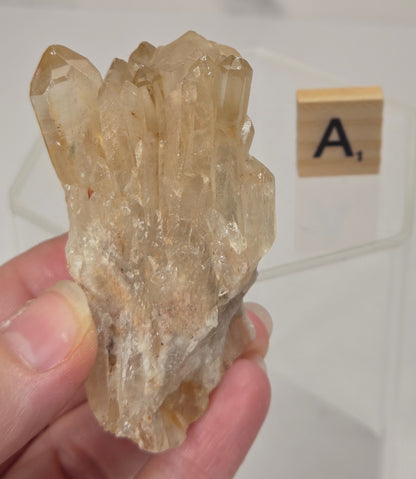 citrine cluster specimen being held in a hand with a wooden letter tile in the background against a white marbled background