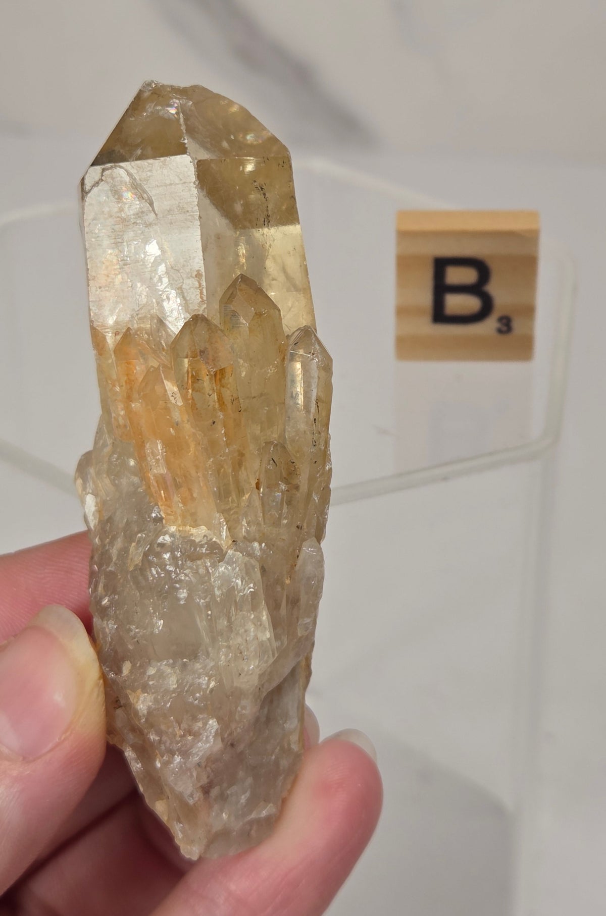 citrine cluster specimen being held in a hand with a wooden letter tile in the background against a white marbled background