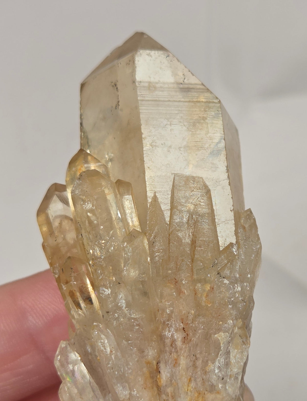 A hand holding a natural quartz crystal cluster with a prominent hexagonal point, showing translucent golden-brown and clear qualities against a plain light background.